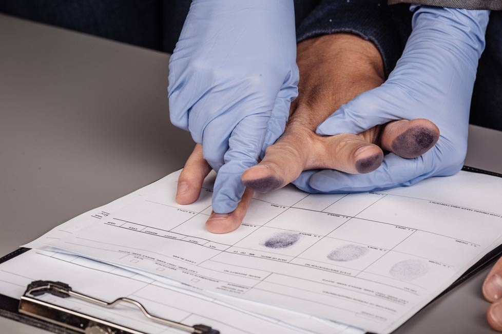 Gloved individual takes fingerprints of another person